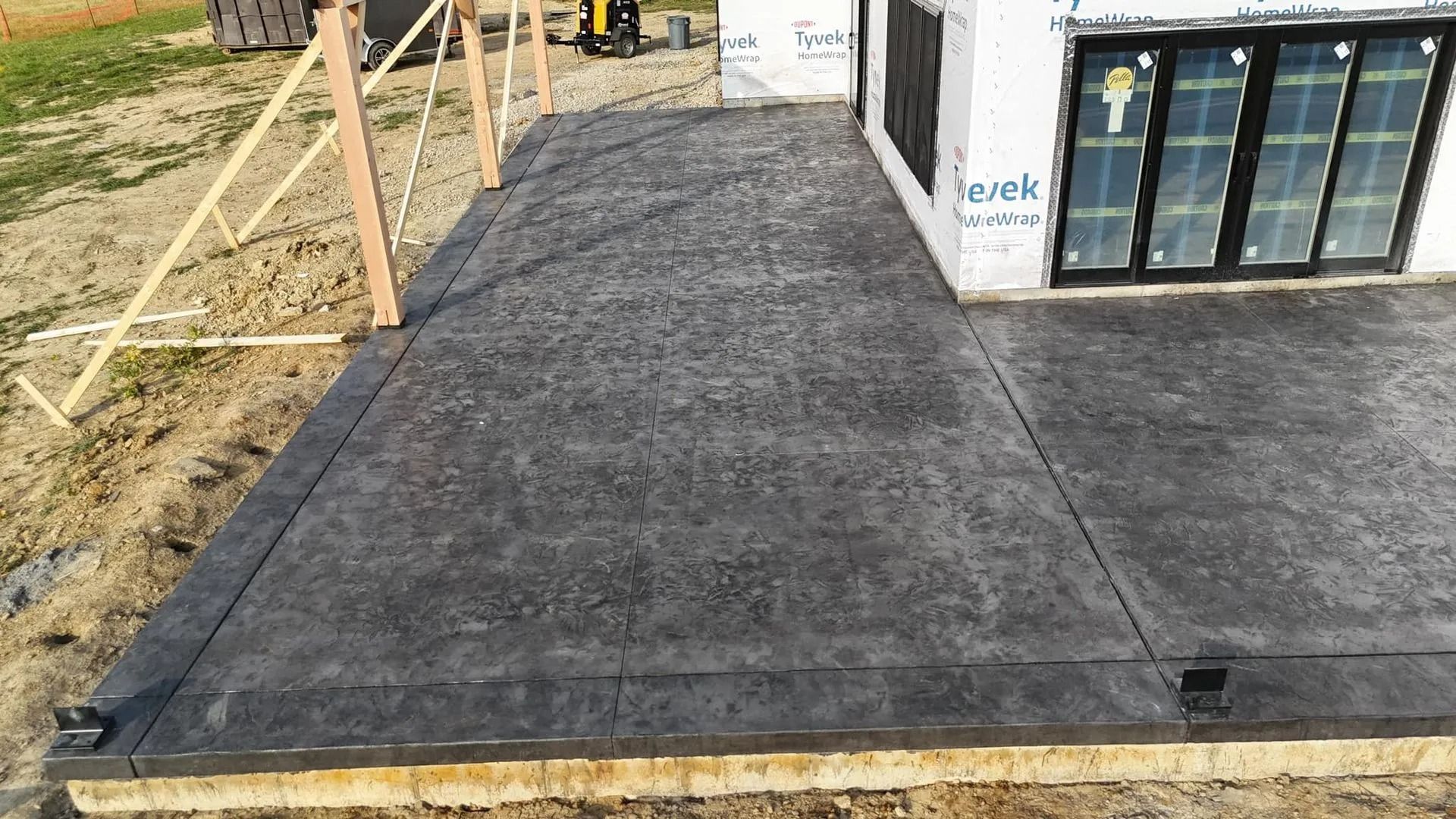 Concrete patio under construction next to a house with large windows.
