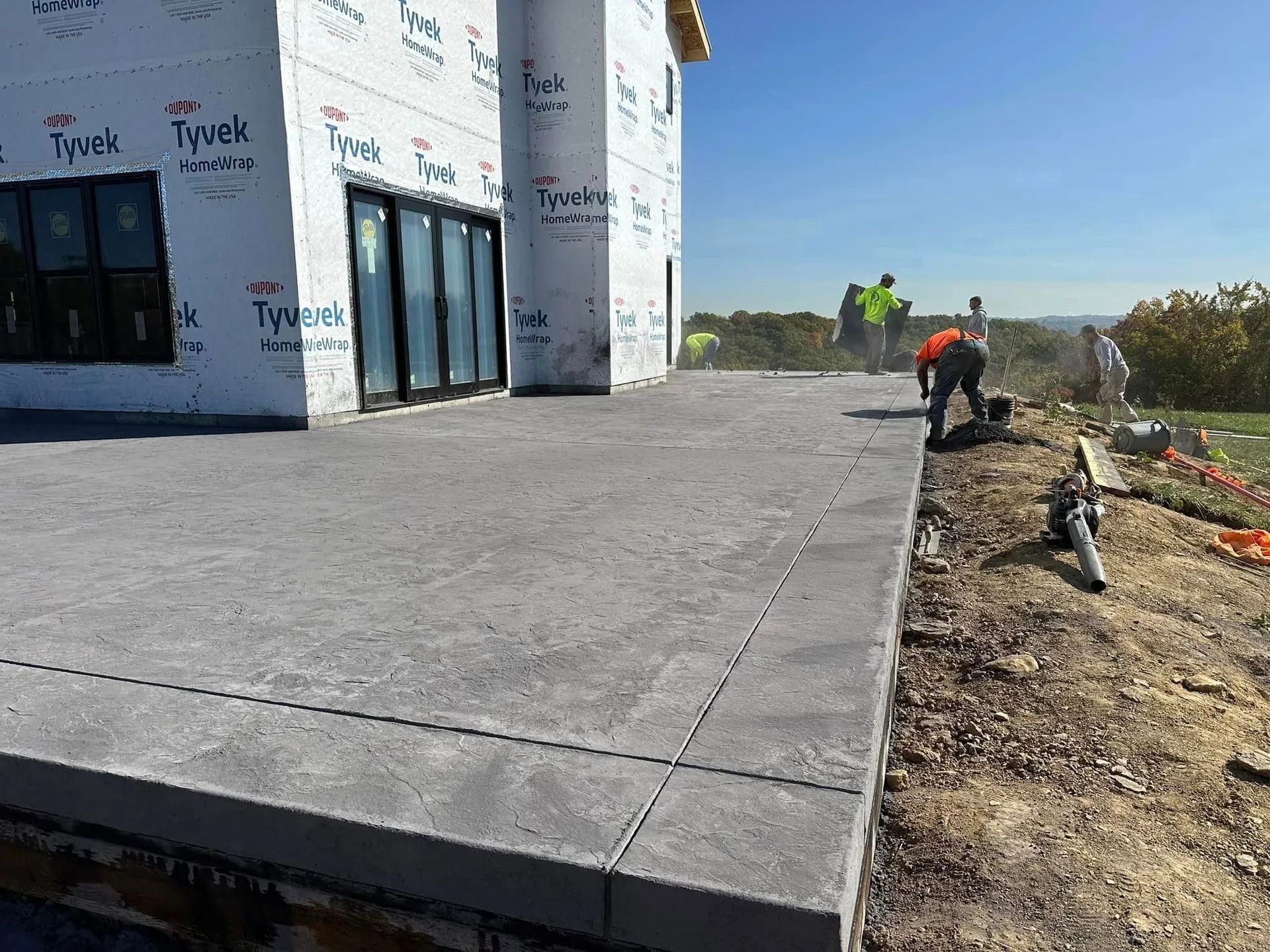 Workers finishing a concrete patio next to a house under construction; sunny day.