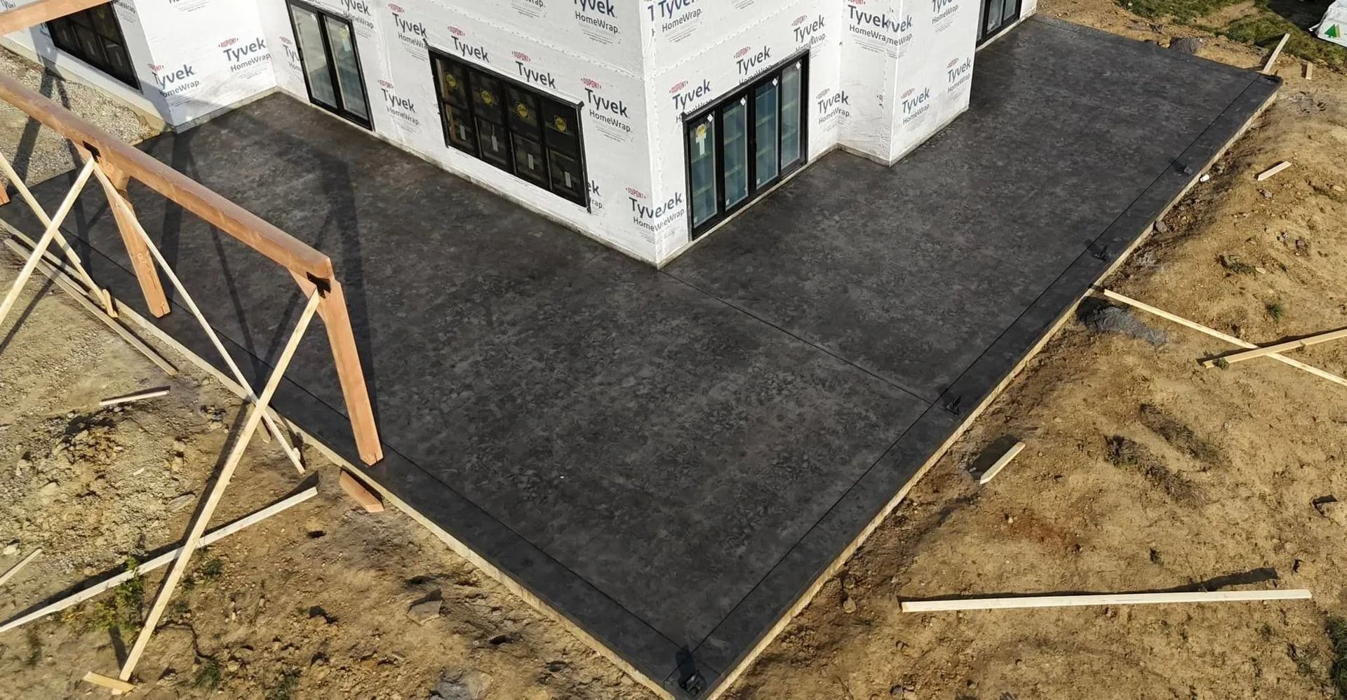 Aerial view of a gray concrete patio and building under construction. Support beams and surrounding dirt are also visible.