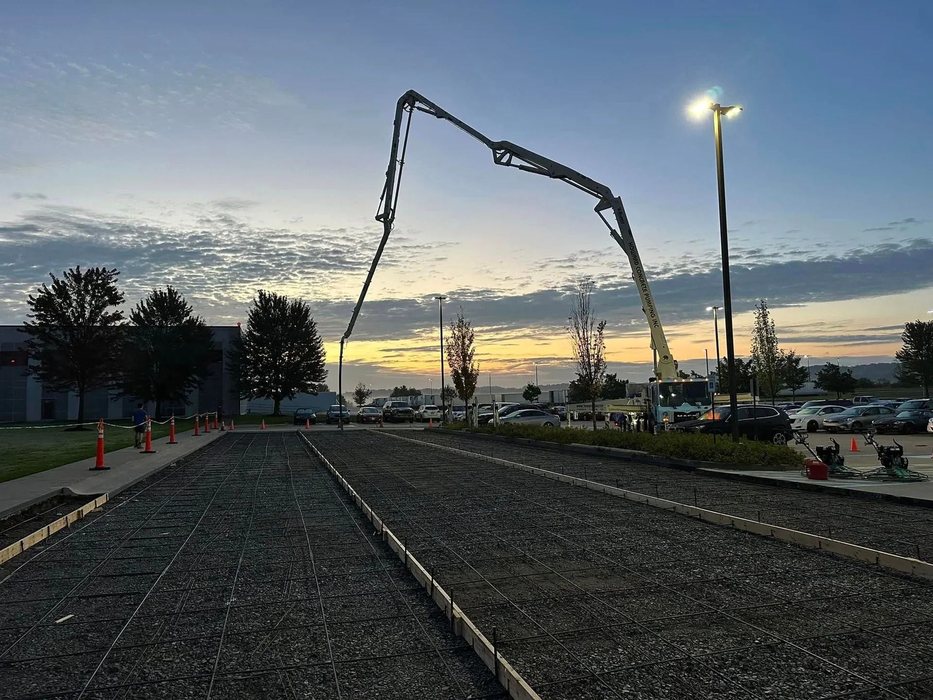 Concrete pour in progress at dusk; concrete pump arm extended over gravel base.