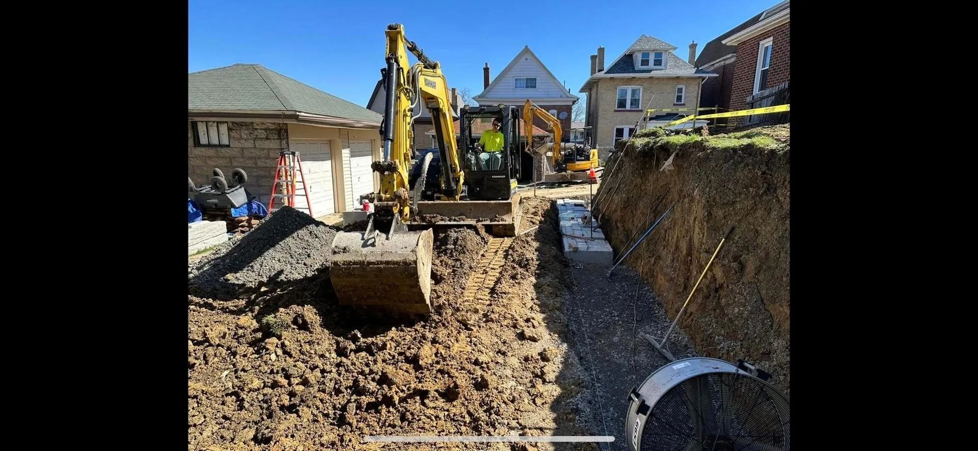 Construction site with yellow excavator digging trench next to a house.