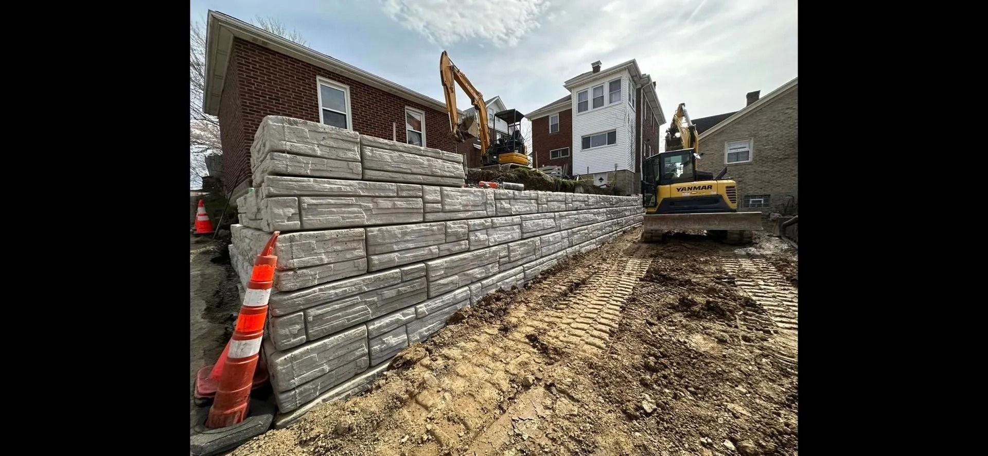 Construction site with a retaining wall being built; excavators in use.