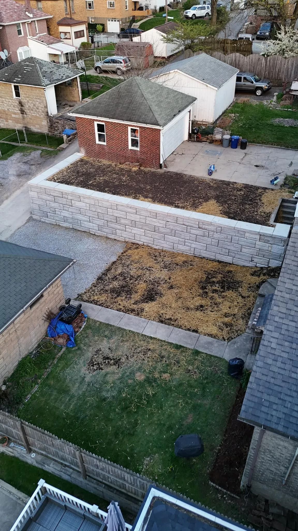 Overhead view of several backyards with a tiered retaining wall, garages, and houses.