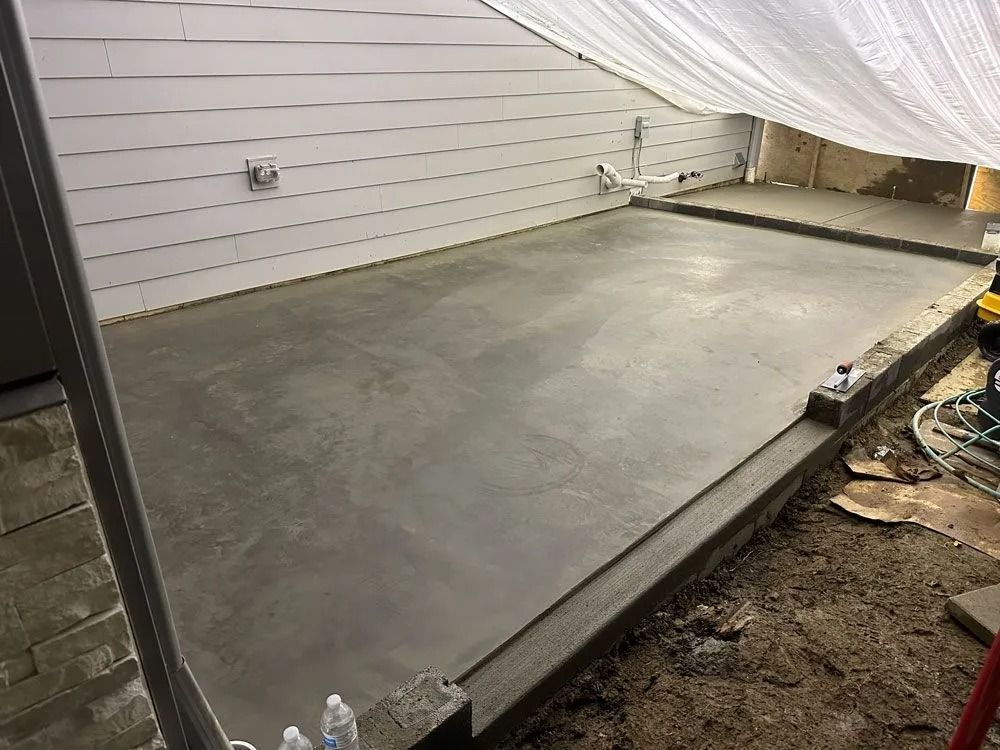 Newly poured concrete patio next to a house with white siding, covered by a white tarp.