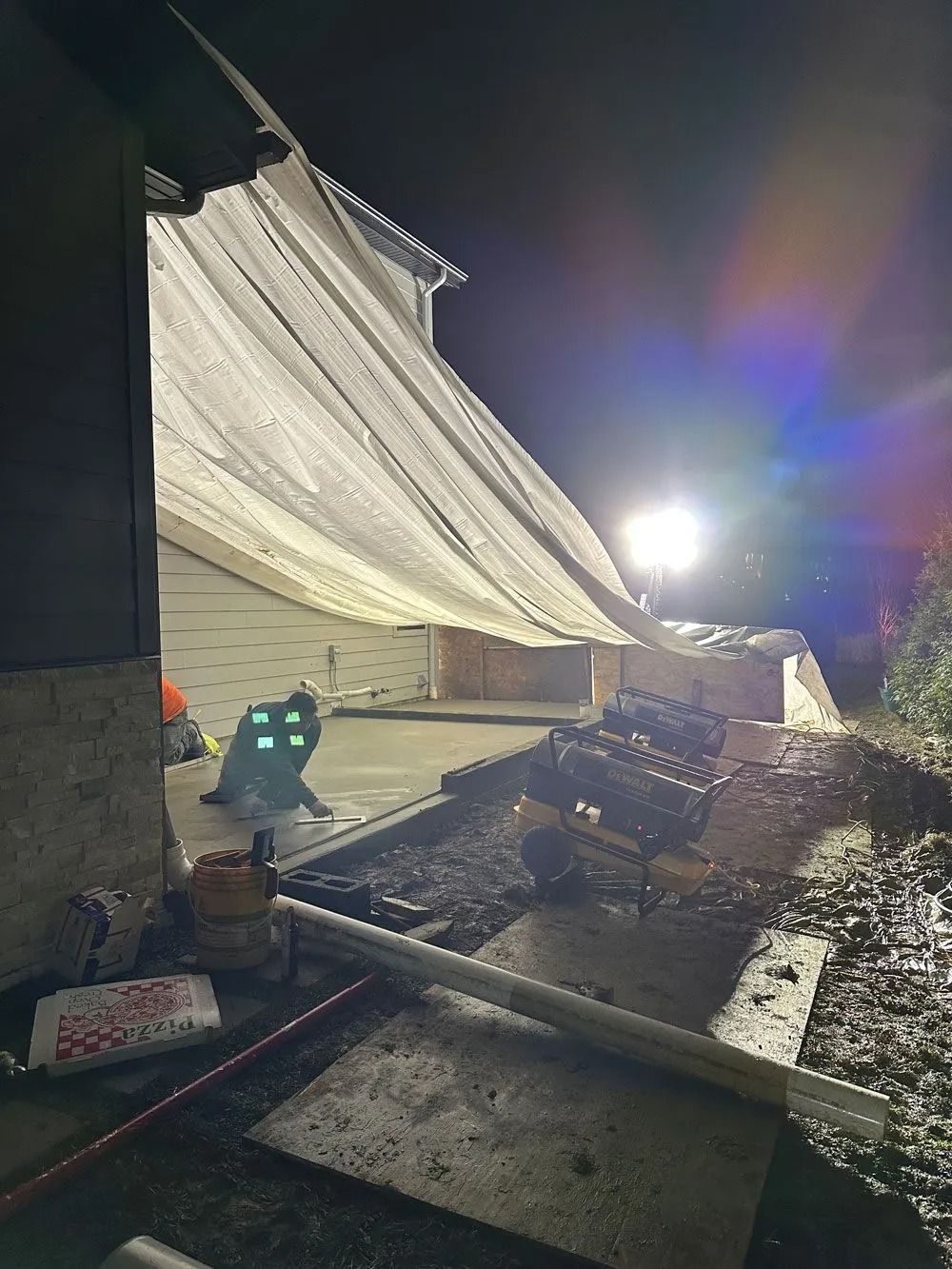 Construction workers pouring concrete at night, under a large white tarp.