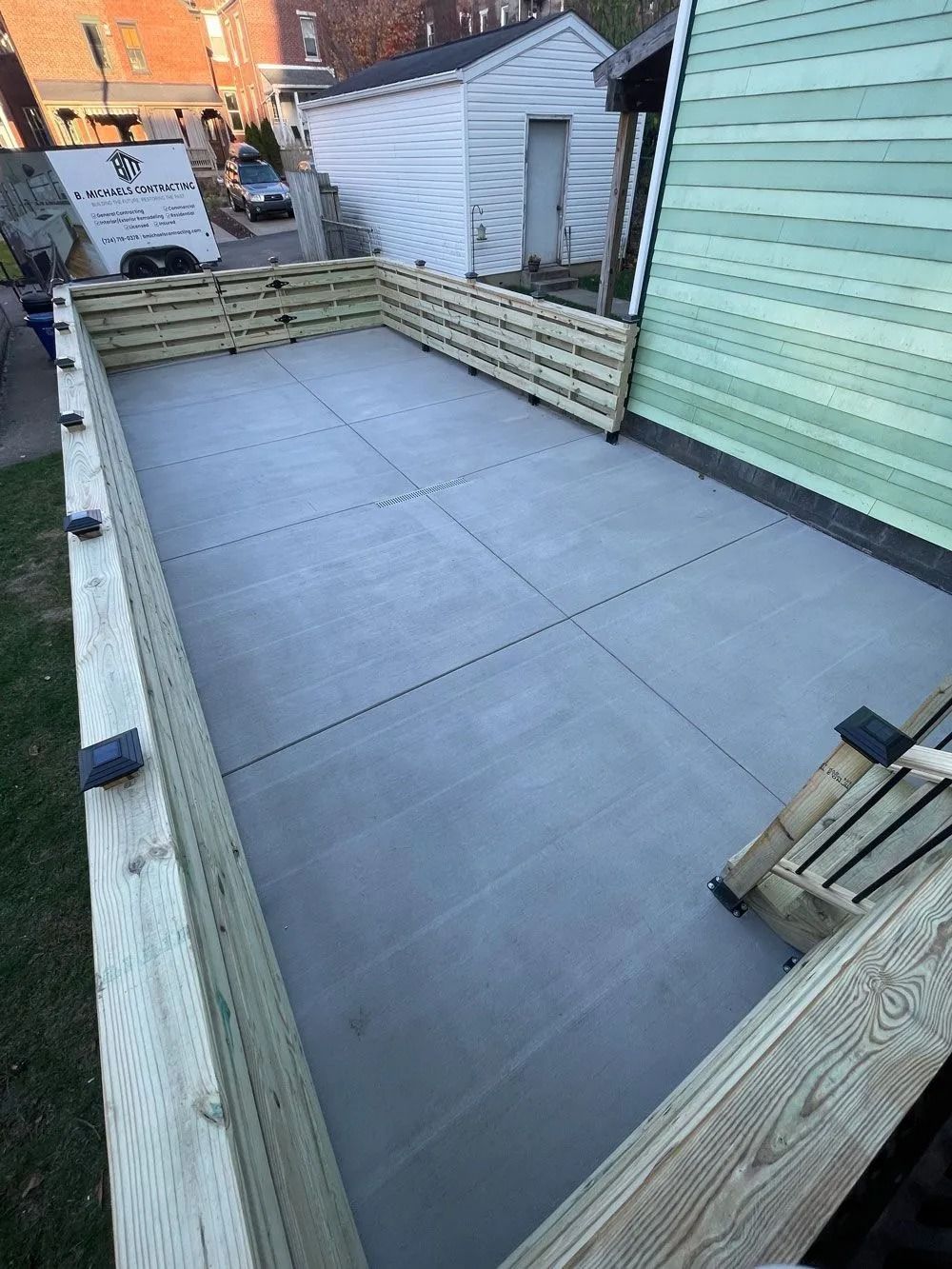 A concrete patio with wood fencing and steps, adjacent to a green-sided house.