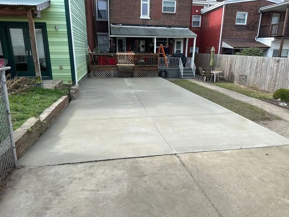 Concrete driveway leading to a house with a porch. Green lawn and a wooden fence on either side.