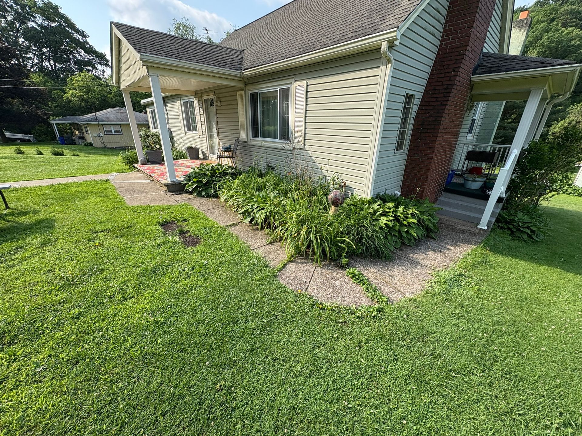 A house with a green lawn and a garden in front. A chimney is visible on the side.