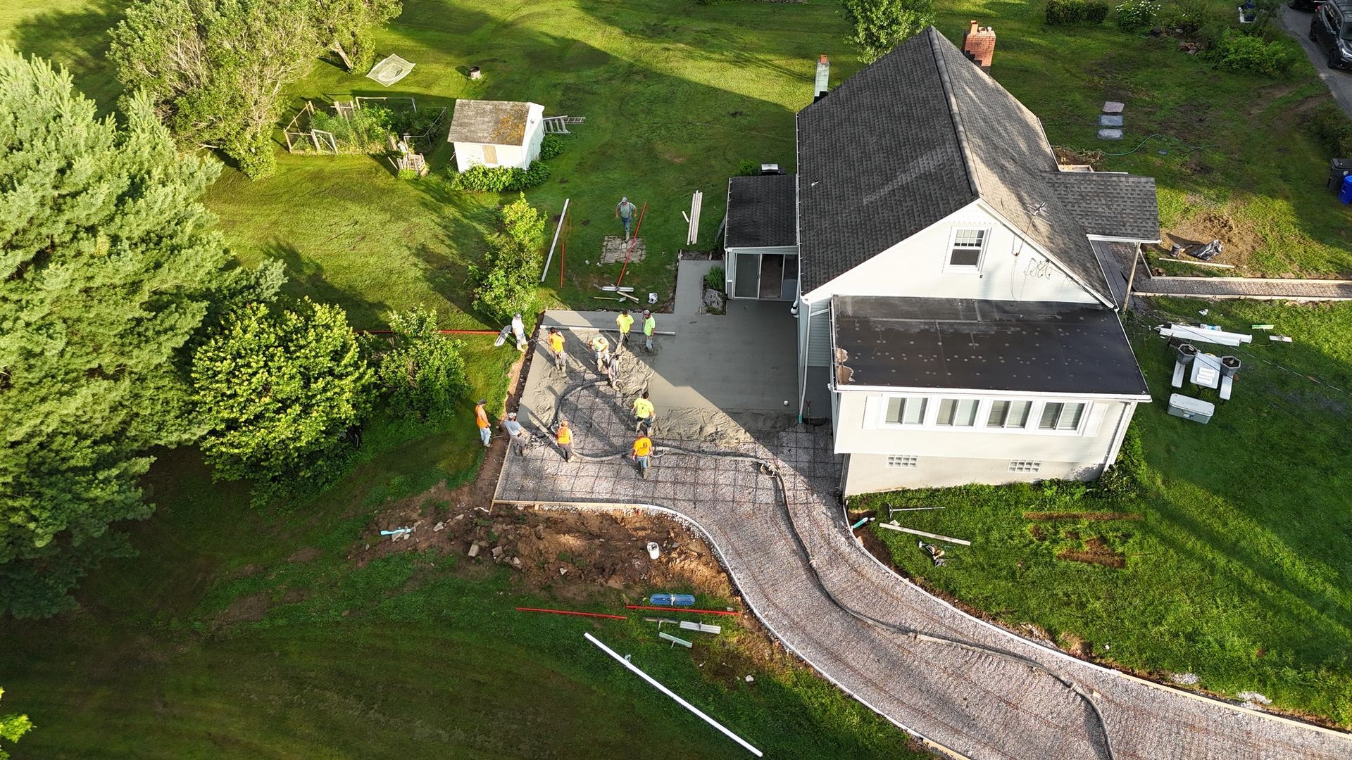 Aerial view of a house and driveway under construction; workers in yellow vests stand near the driveway.