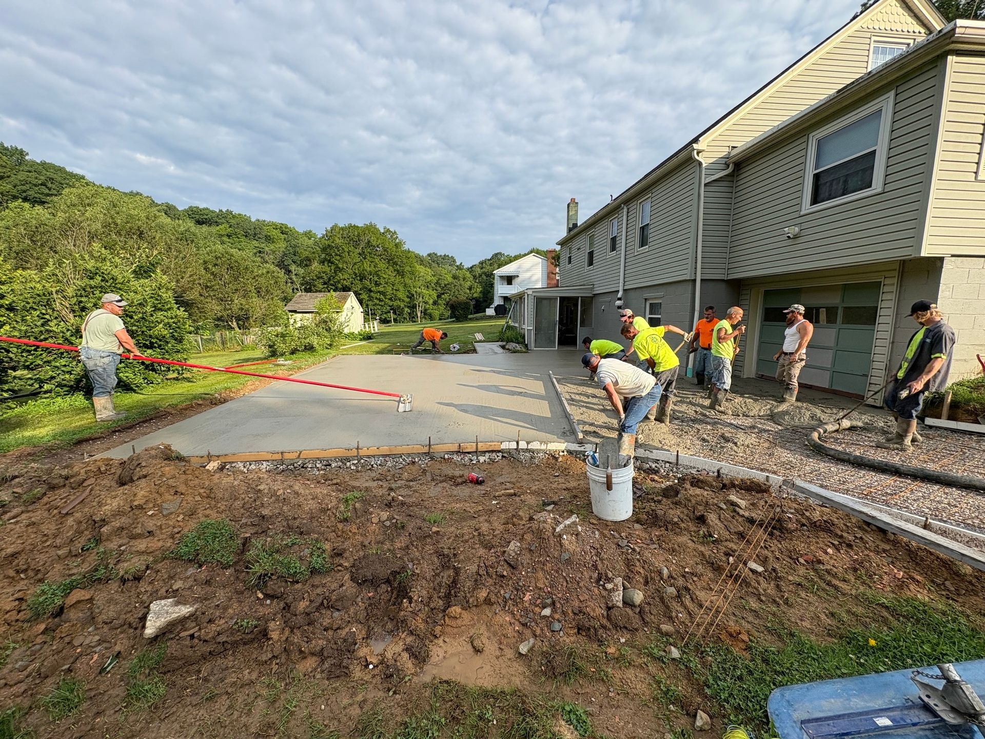 Construction workers pouring concrete for a patio next to a two-story house.