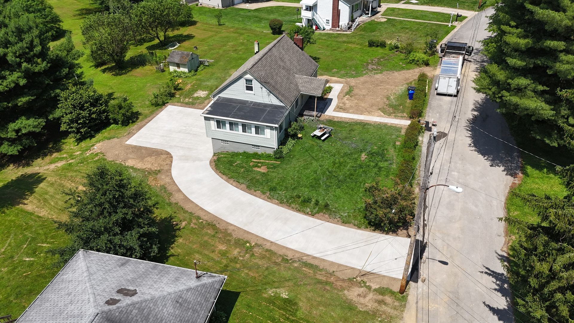 Aerial view of a gray house with a concrete driveway and a street with a vehicle.