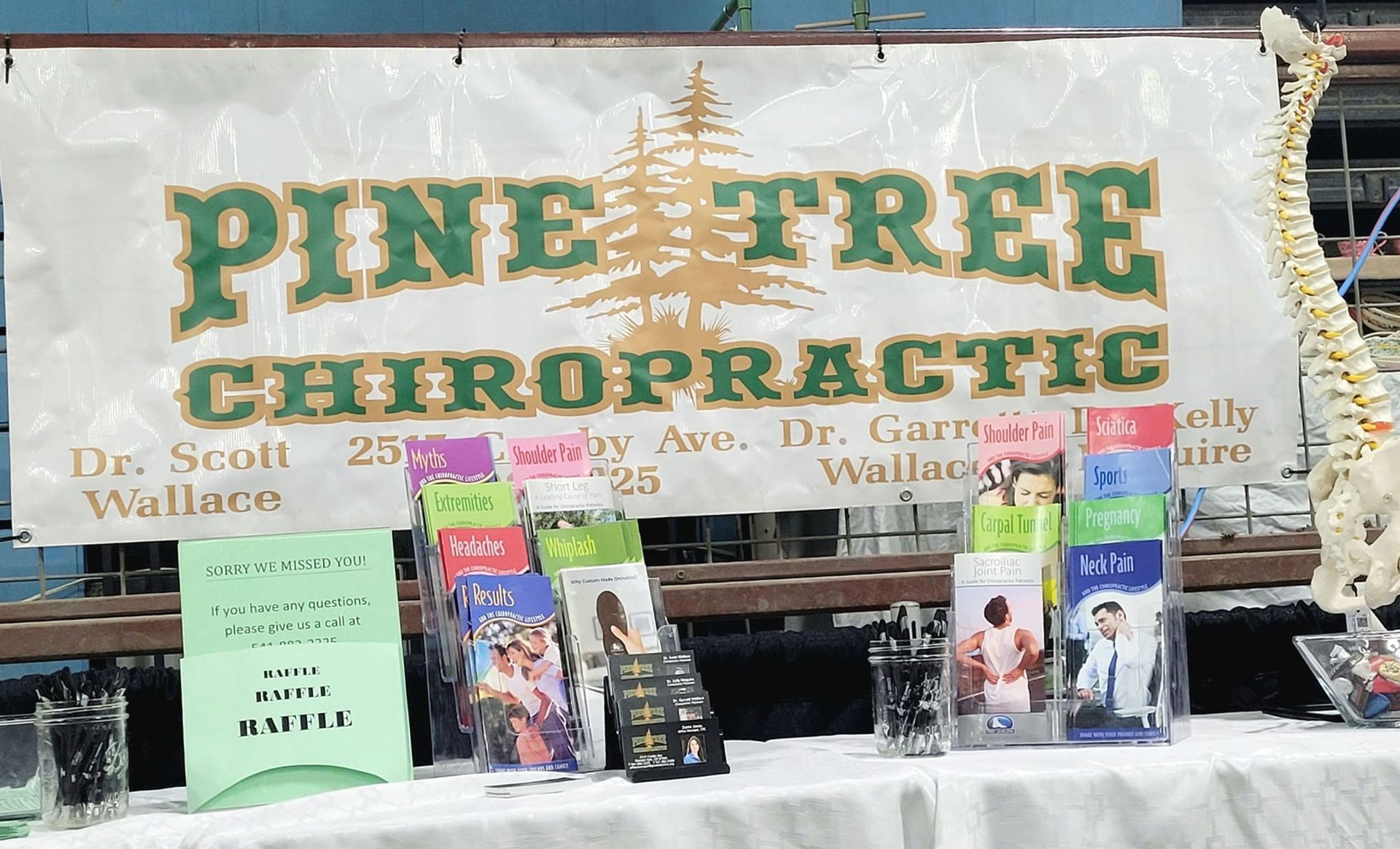 Pine Tree Chiropractic booth with brochures, spinal model, and banner with green and gold logo.