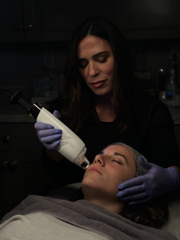A woman is giving a woman a facial treatment in a dark room.