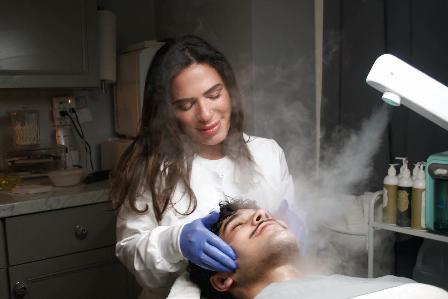 A woman is giving a man a steam treatment on his face.