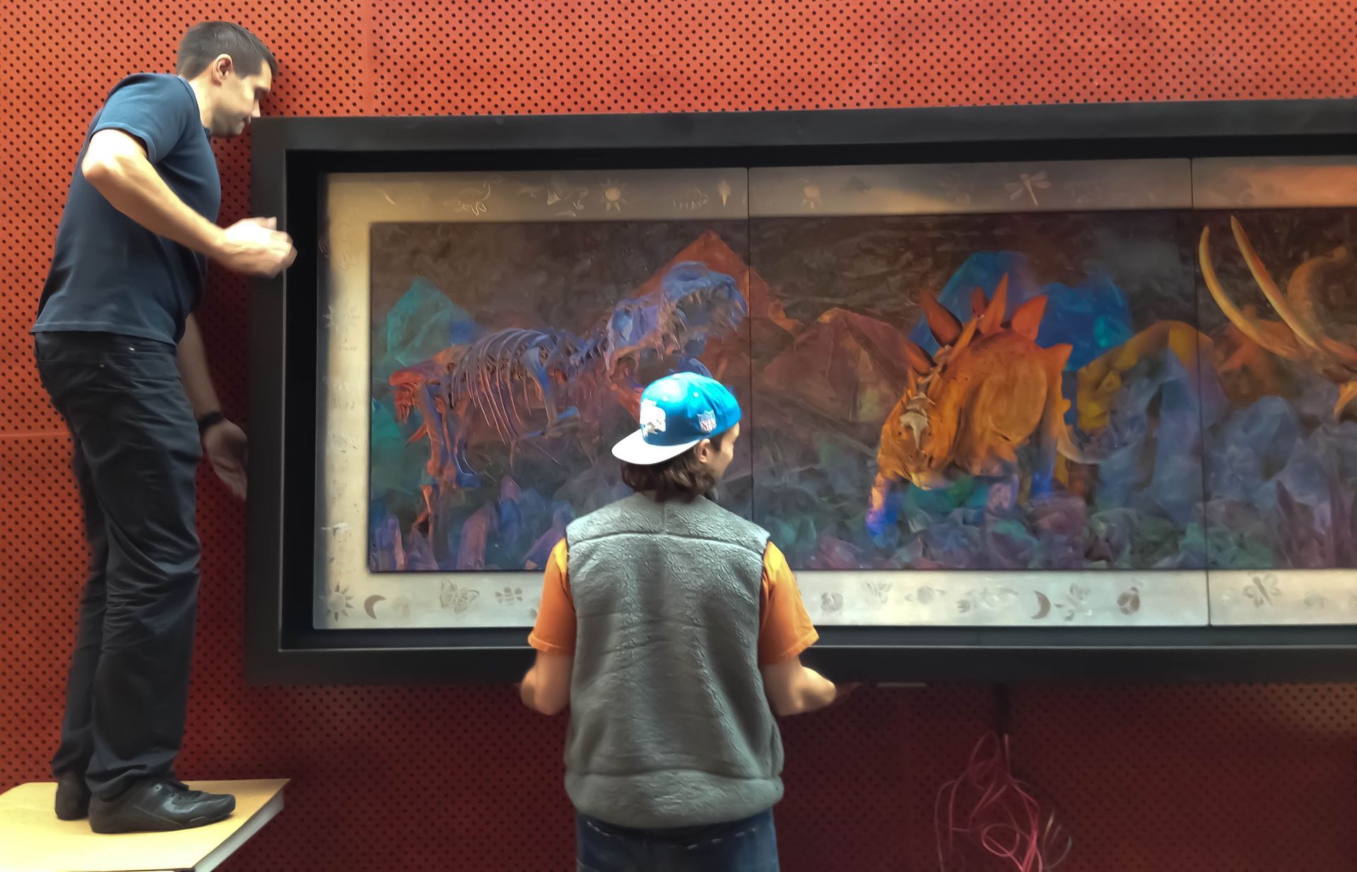 A man and a boy are looking at a painting on a wall.