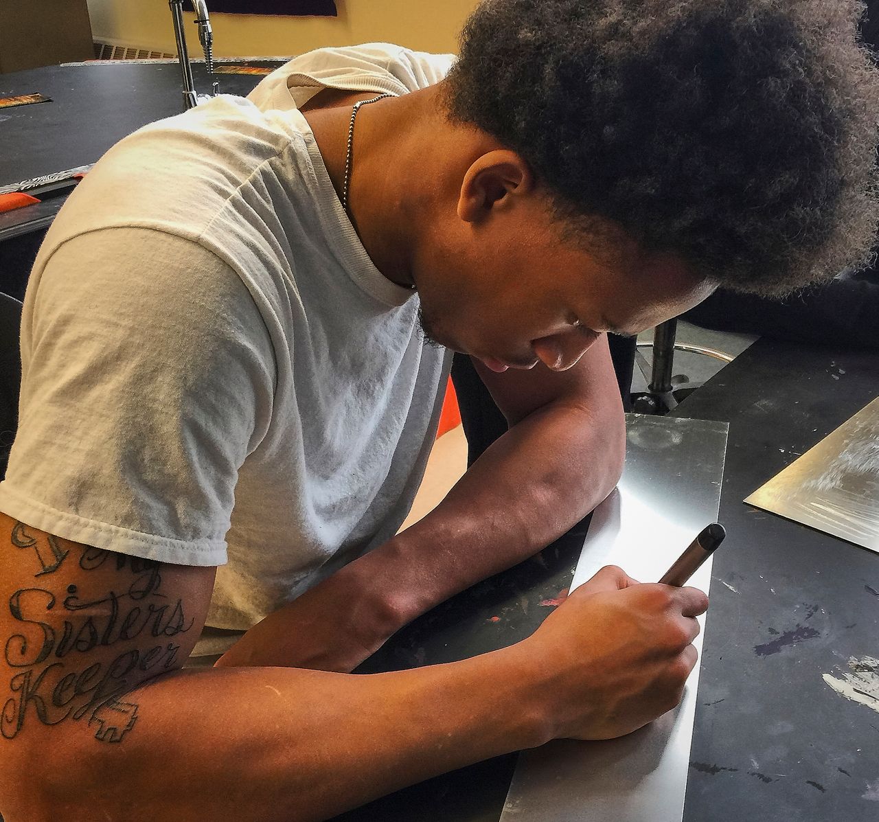 A man with a tattoo on his arm is writing on a piece of paper