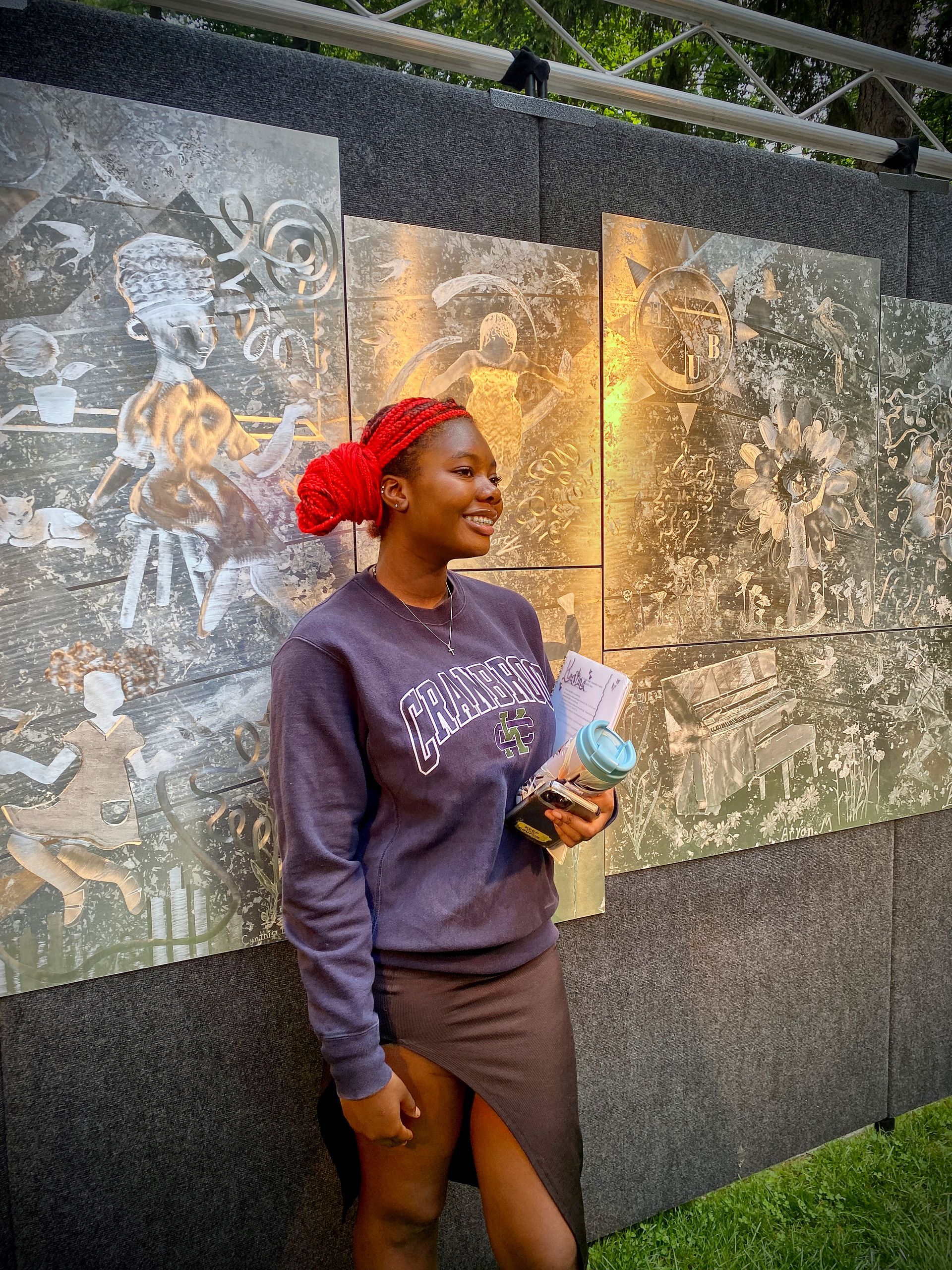 A woman wearing a sweatshirt and a skirt is standing in front of a wall.