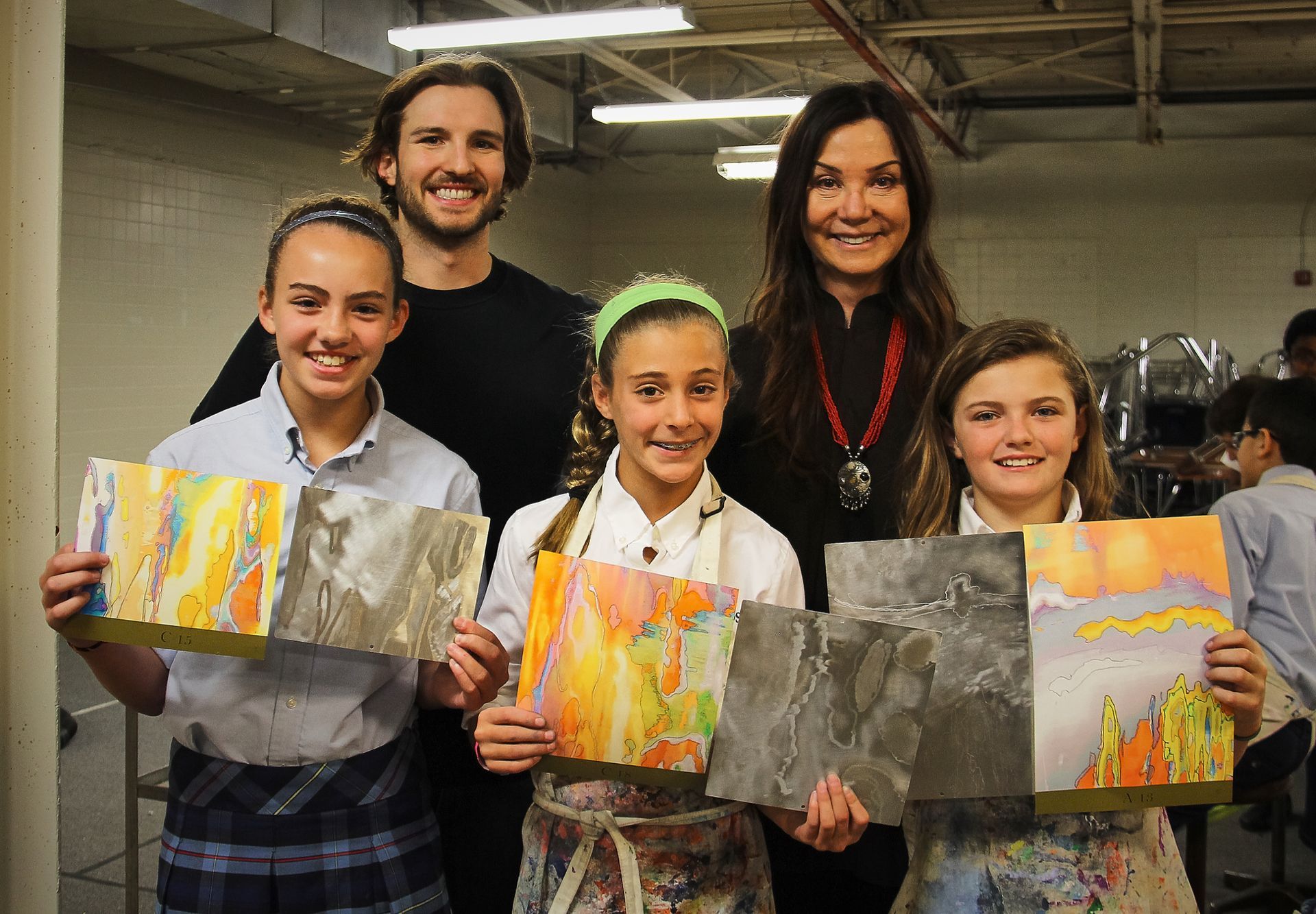 A group of people are standing next to each other holding paintings.
