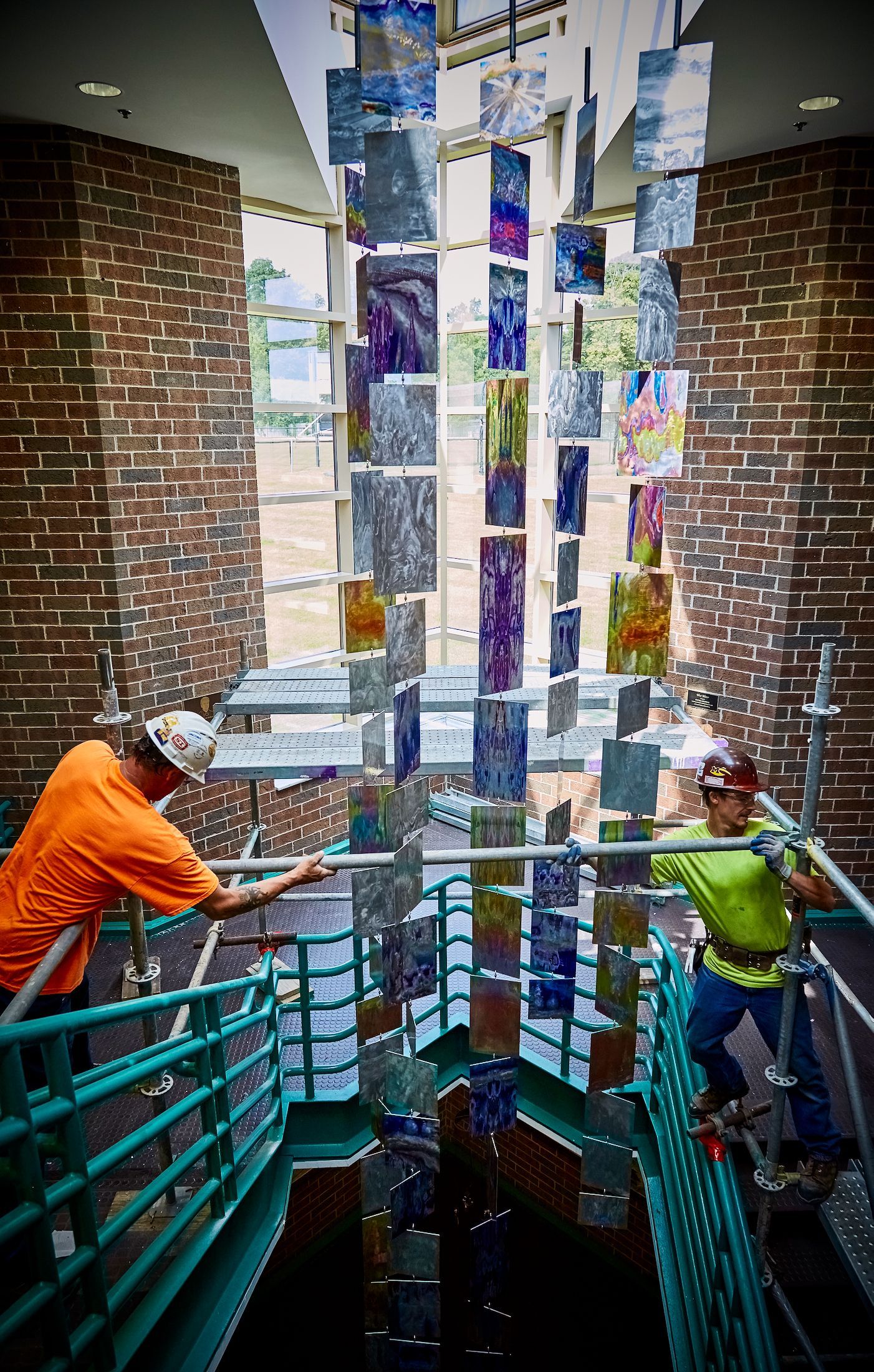 Two men are working on a stained glass sculpture in a building.