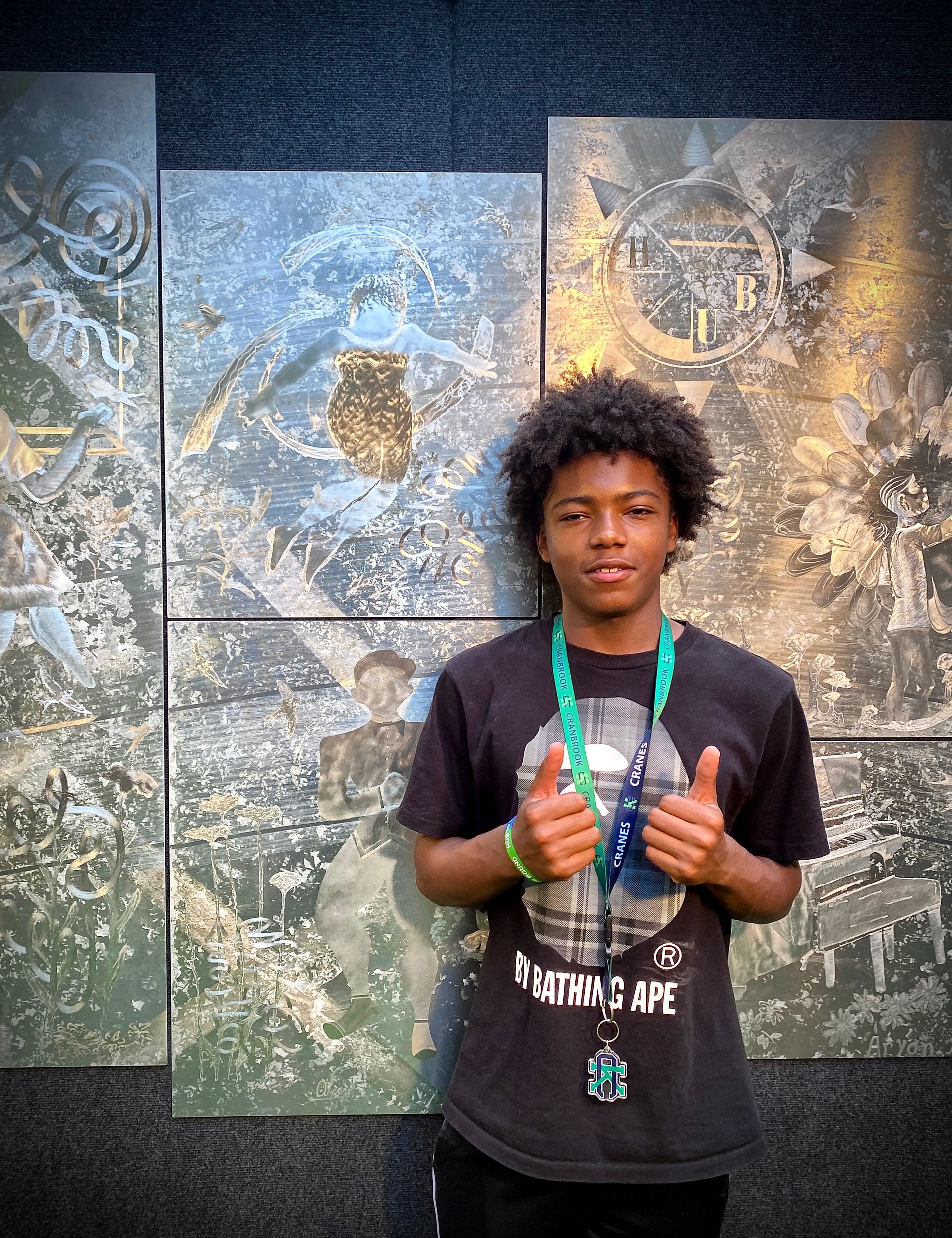A young man is giving a thumbs up in front of a painting.