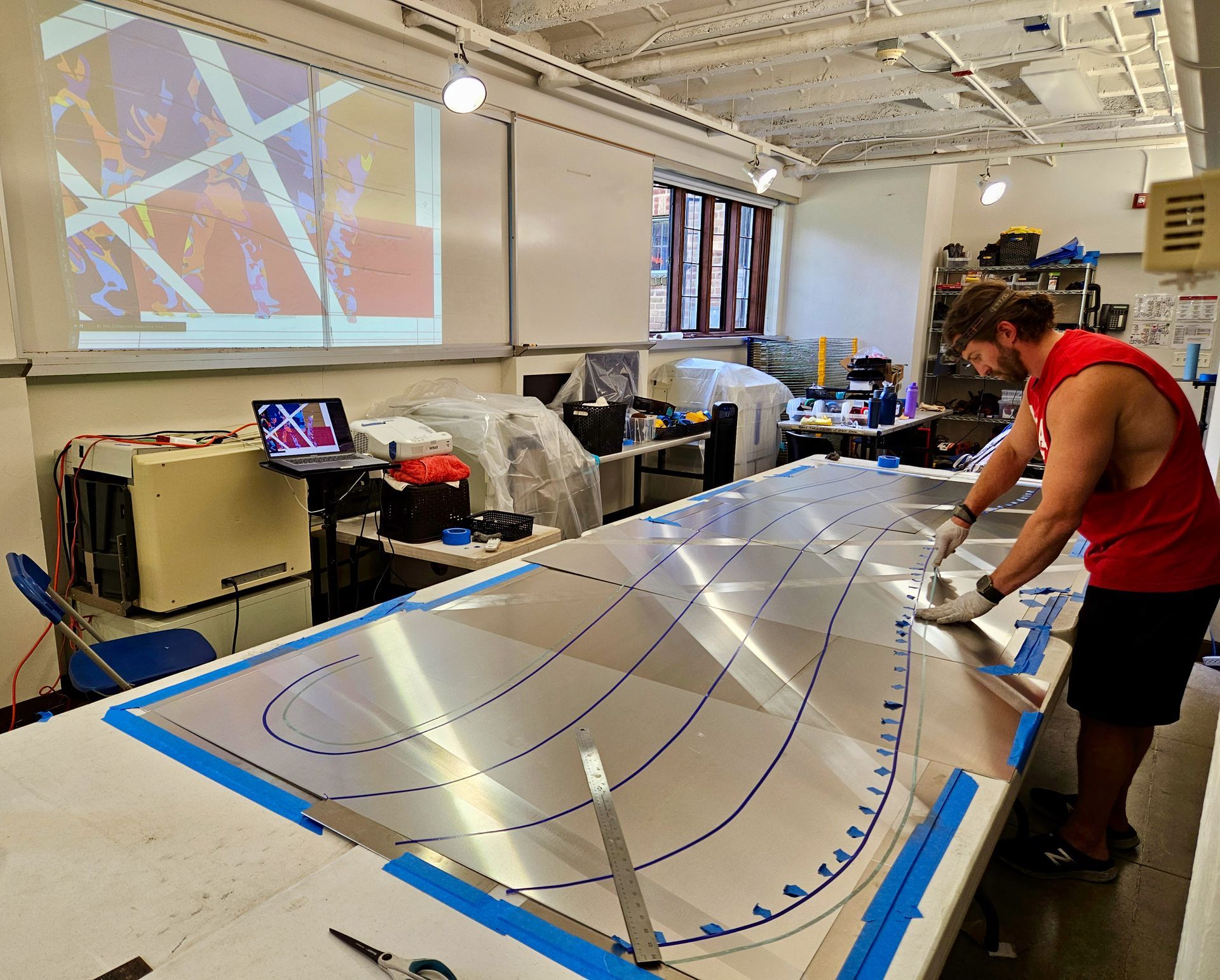 A man in a red tank top is working on a large piece of metal