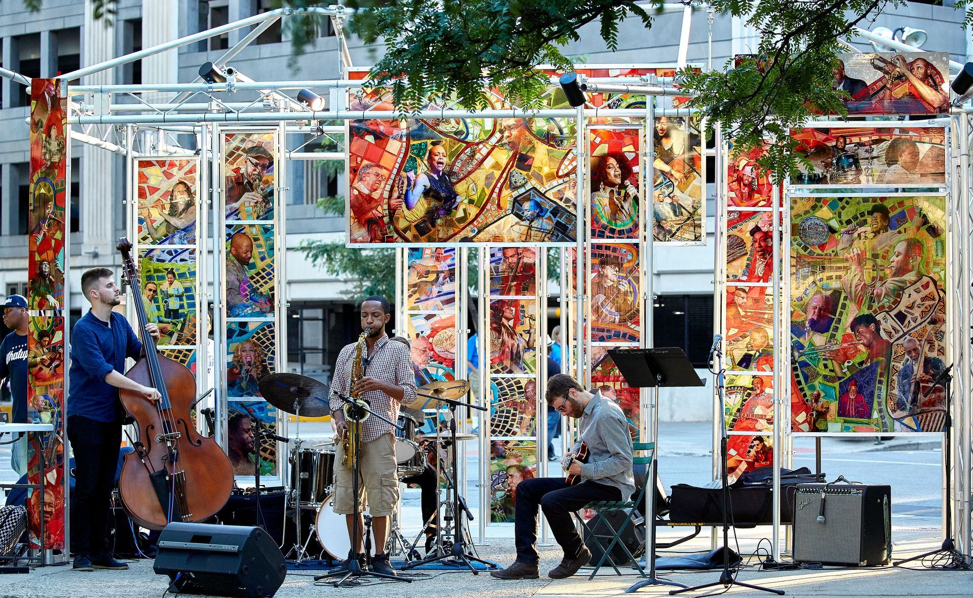 A group of people are playing instruments on a stage in front of a painting.