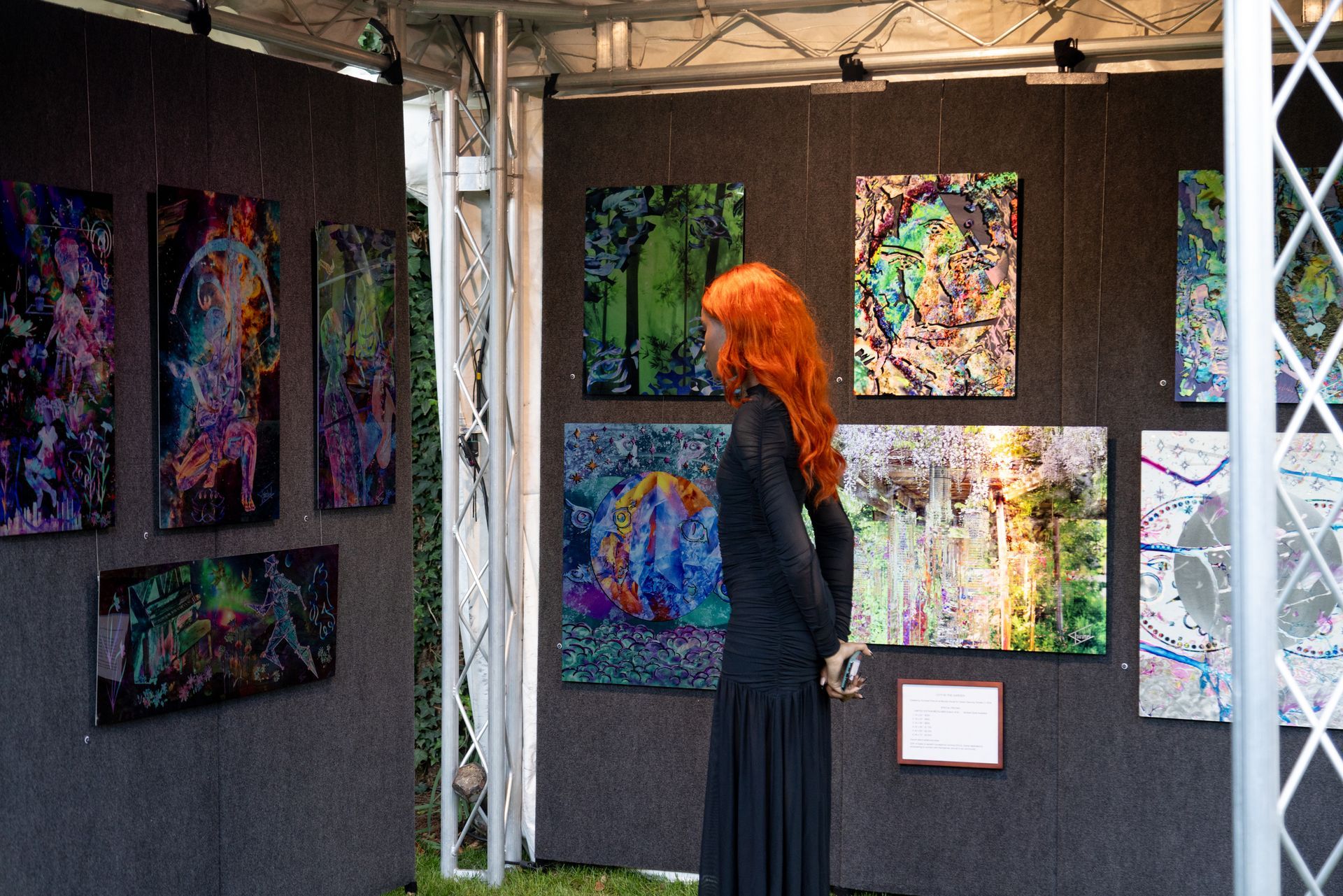 A woman with red hair is standing in front of a wall of paintings.