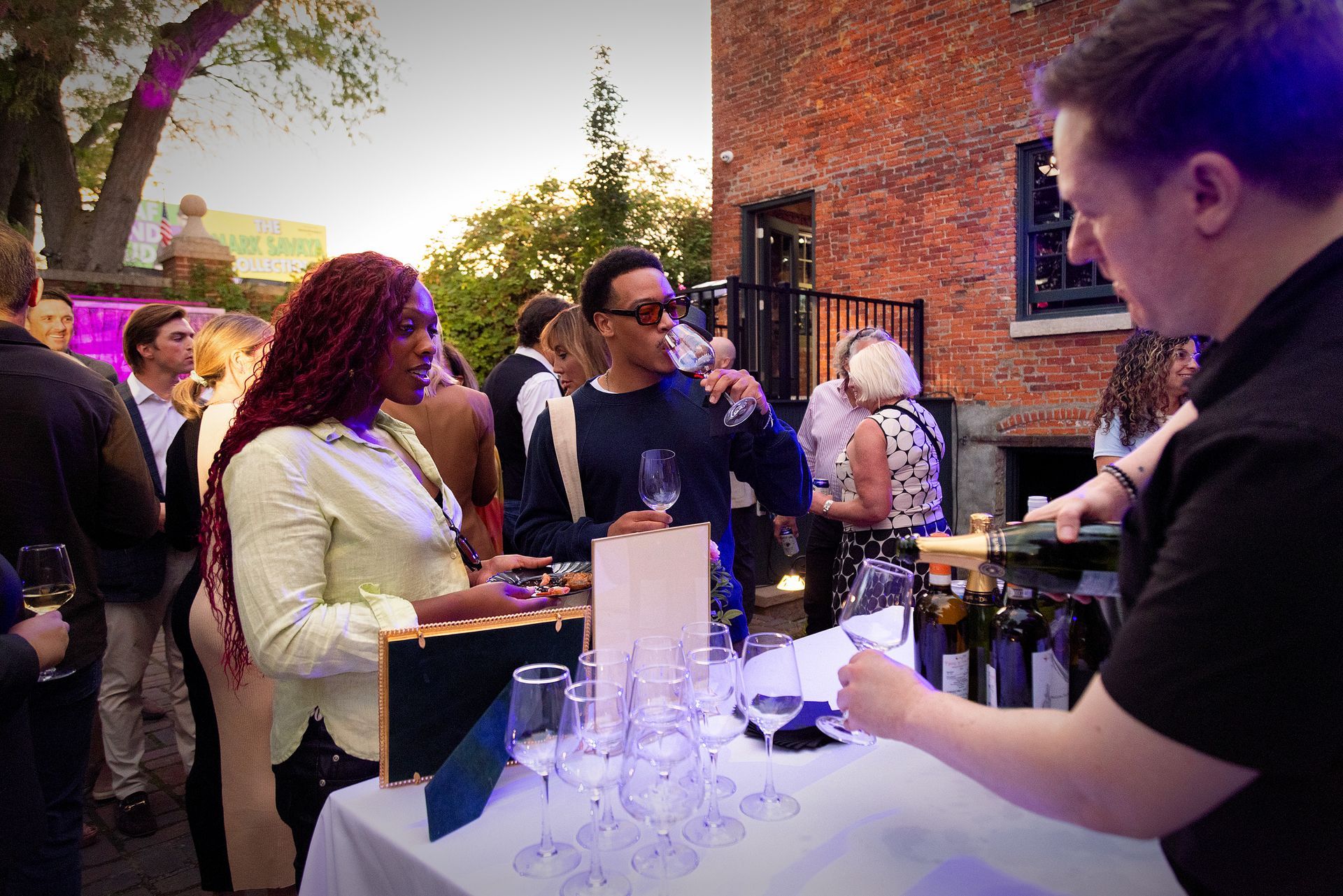 A group of people are standing around a table drinking wine.