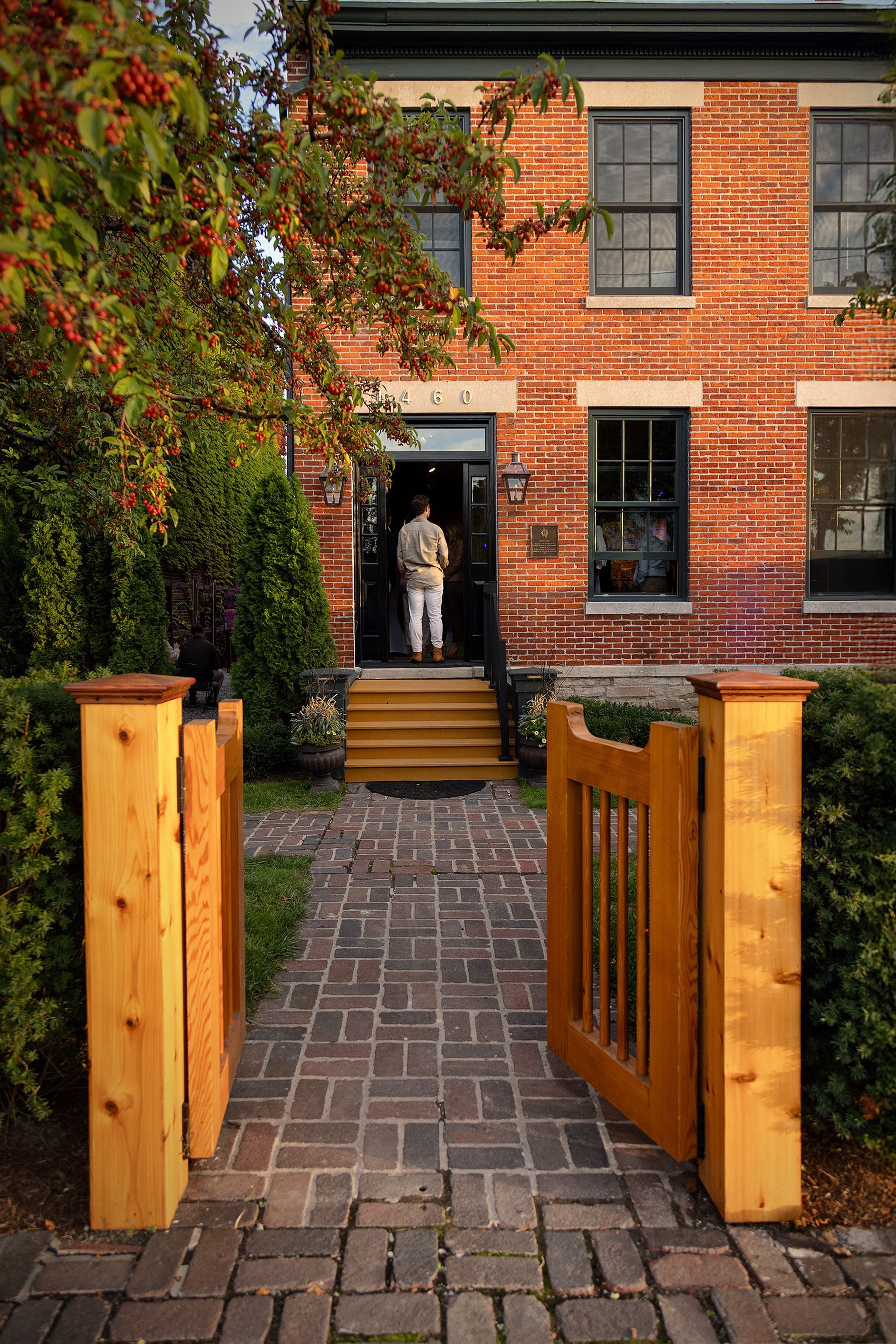 A man is standing in front of a brick house with a wooden gate open.