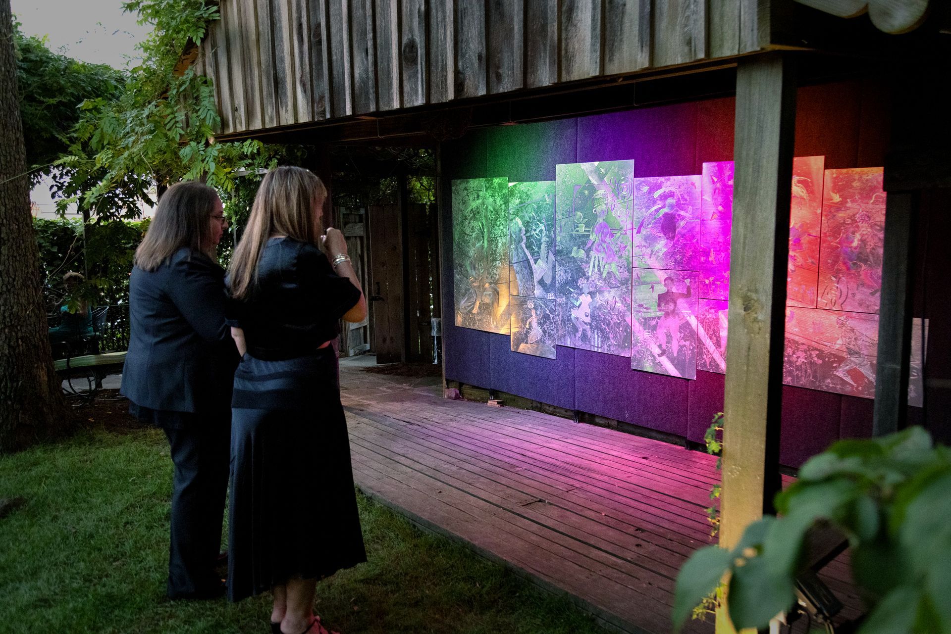 Two women are standing in front of a painting on a wall.