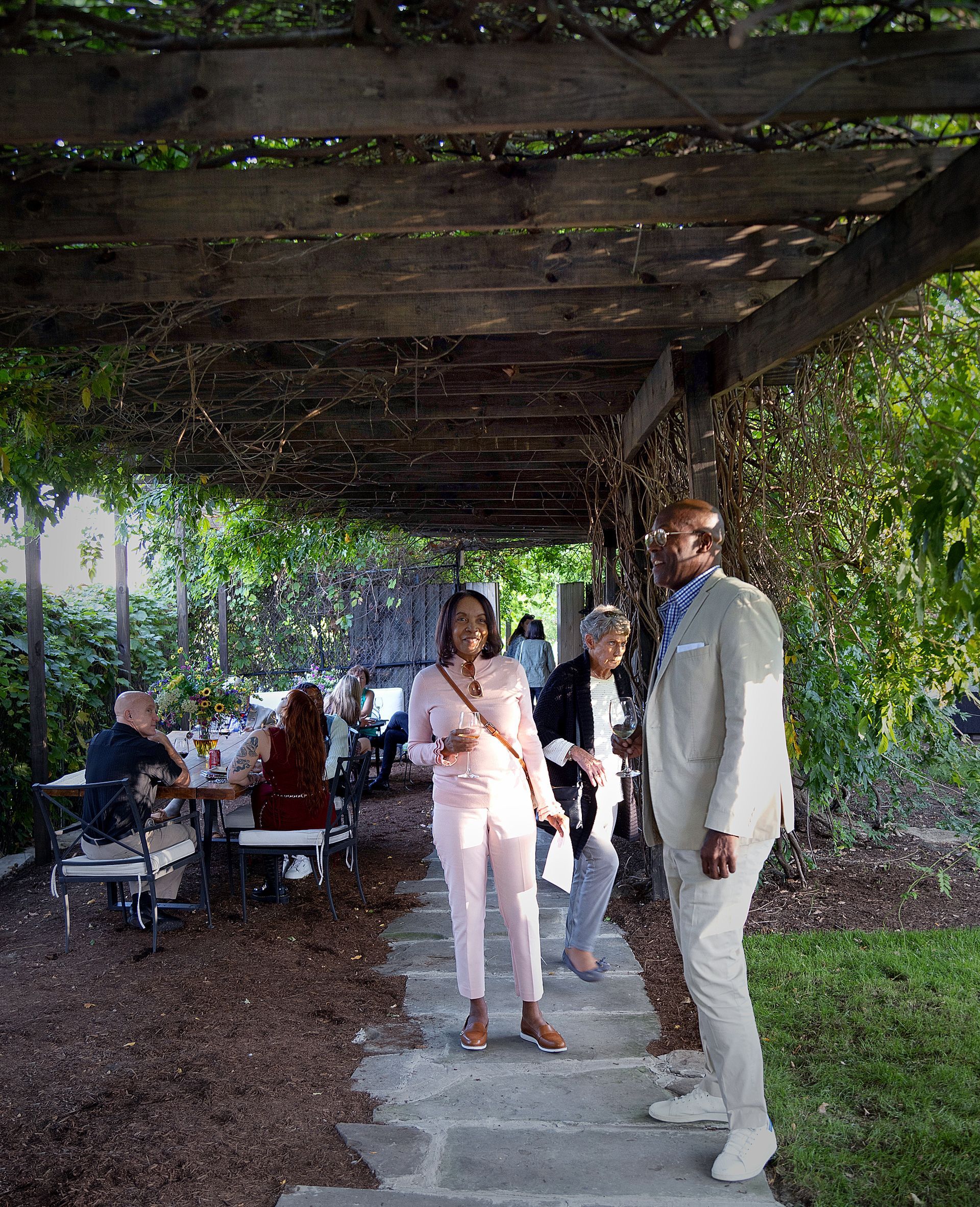 A group of people are standing under a pergola in a garden.