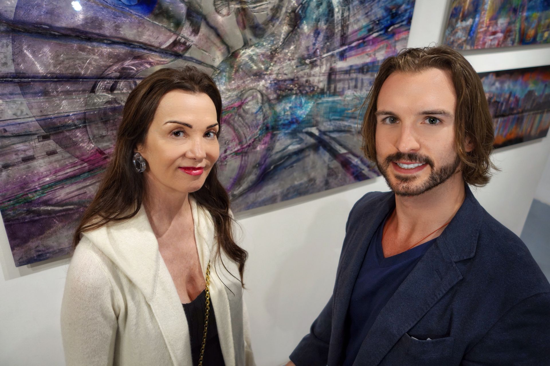 A man and a woman are standing next to each other in front of a painting.