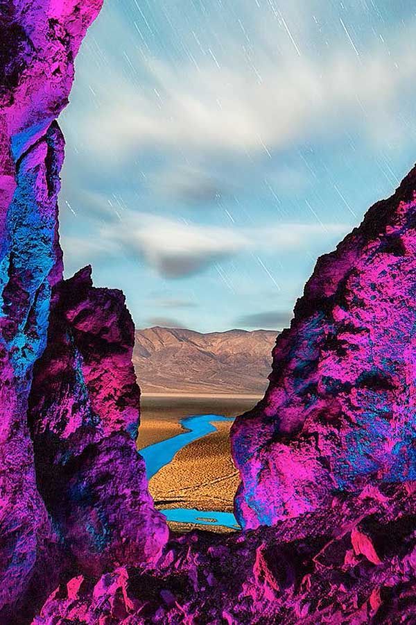 A painting of a river between two rocks with mountains in the background