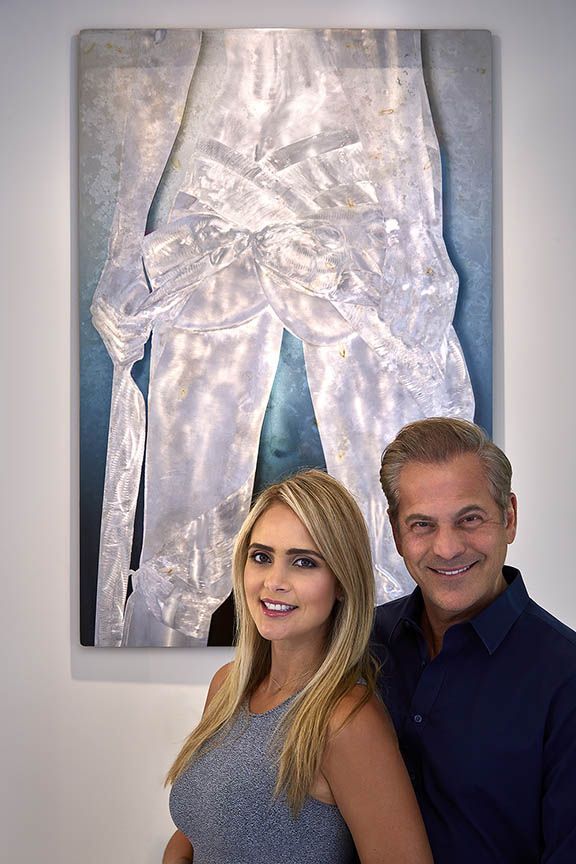 A man and a woman are standing in front of an artwork.