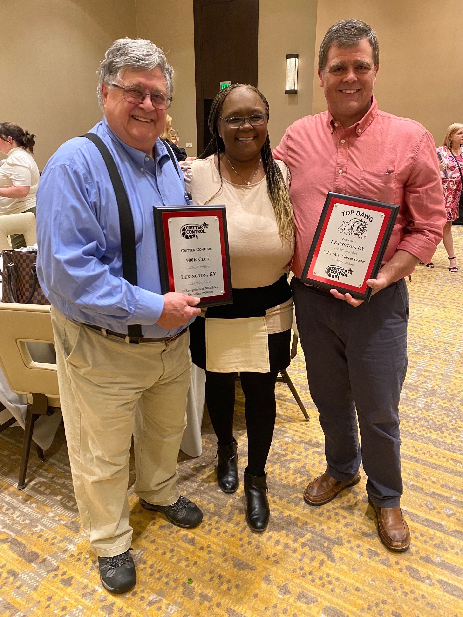 Three people are standing next to each other in a room holding plaques.