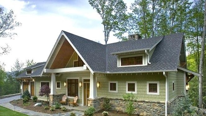 A green house with a gray roof is surrounded by trees