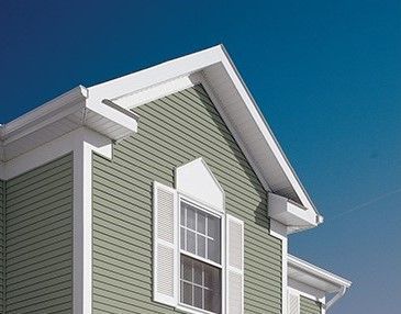 A green house with white trim and shutters against a blue sky