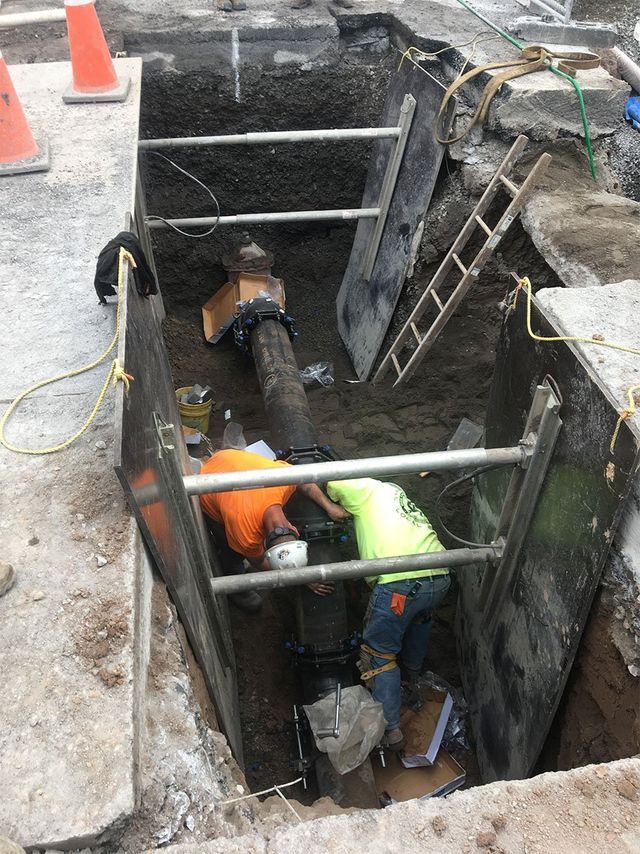 a group of construction workers are working on a pipe in a trench .
