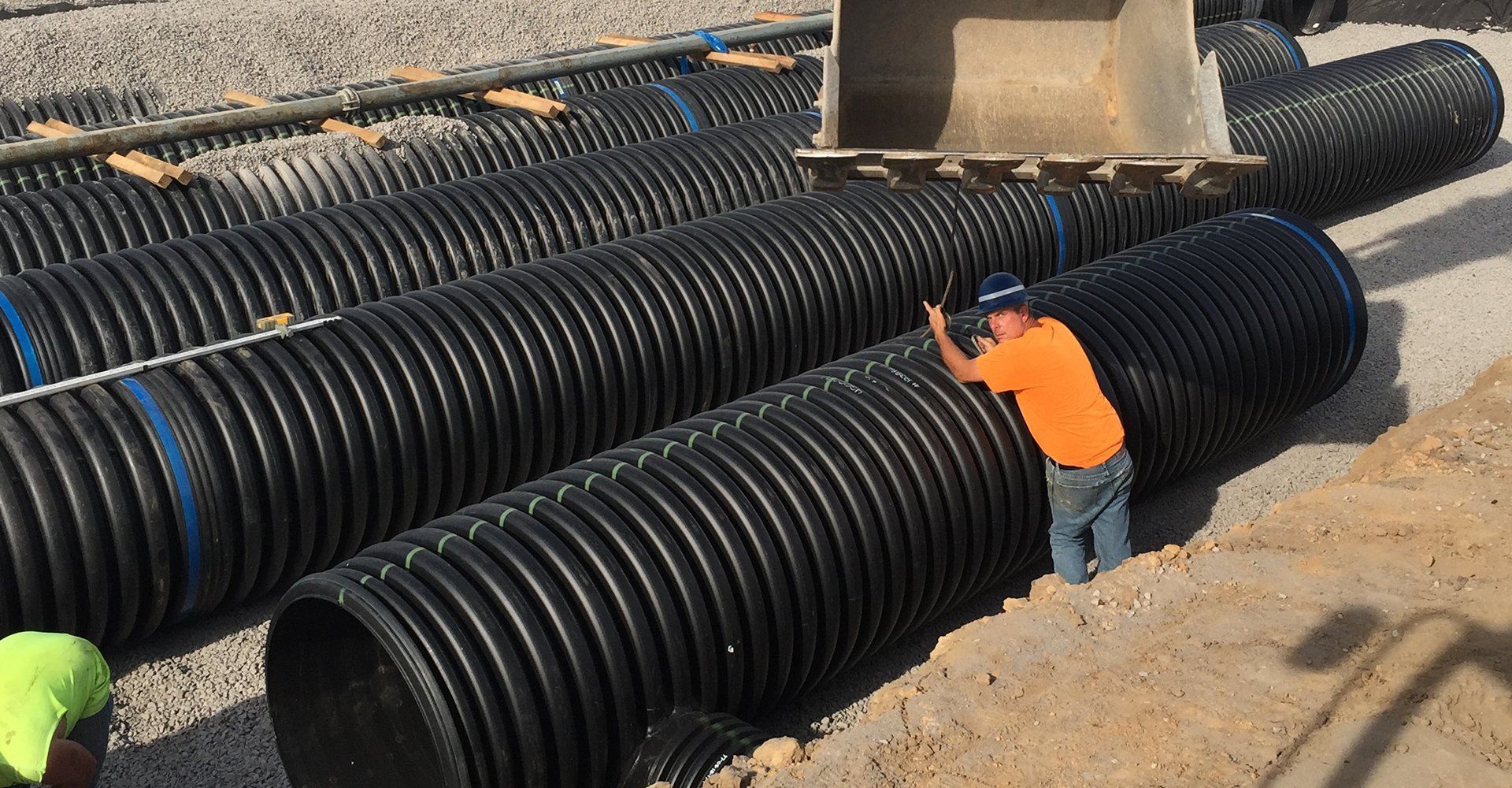 a man in an orange shirt is standing next to a large black pipe .