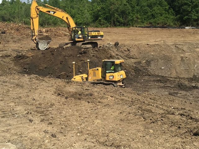 a bulldozer and an excavator are working on a dirt field .