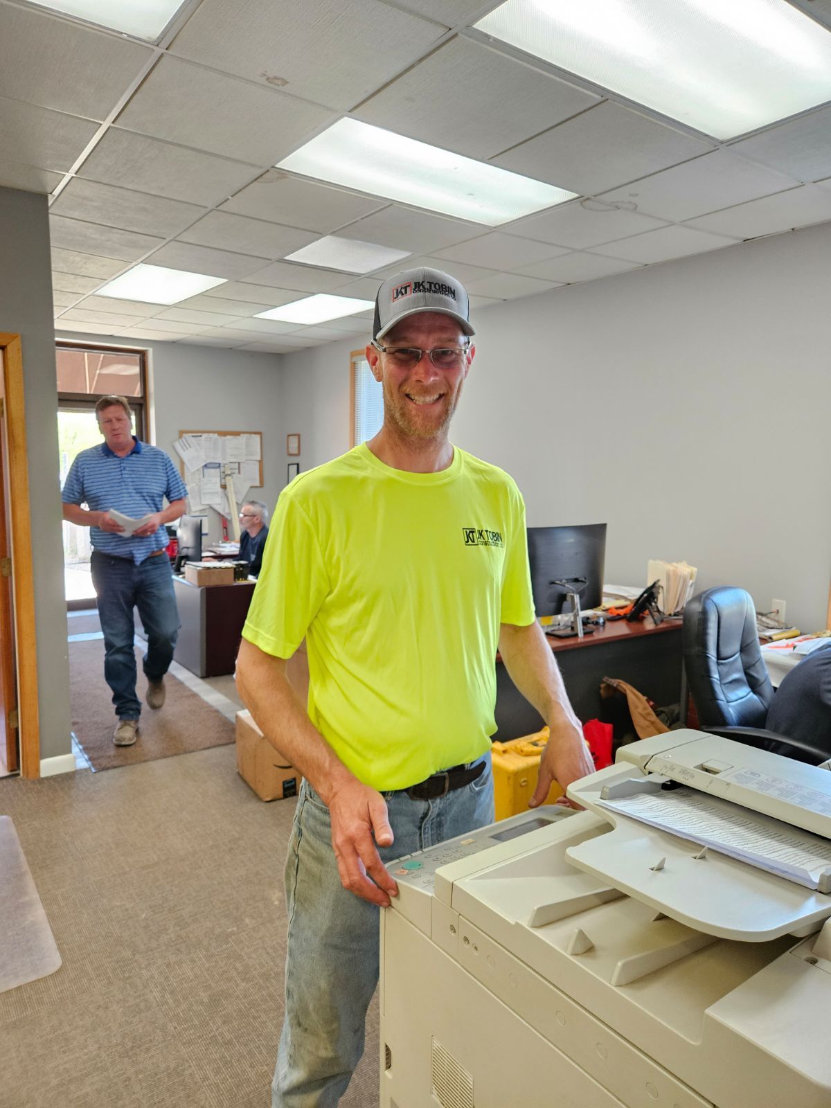 a man in a neon yellow shirt is standing next to a printer in an office .