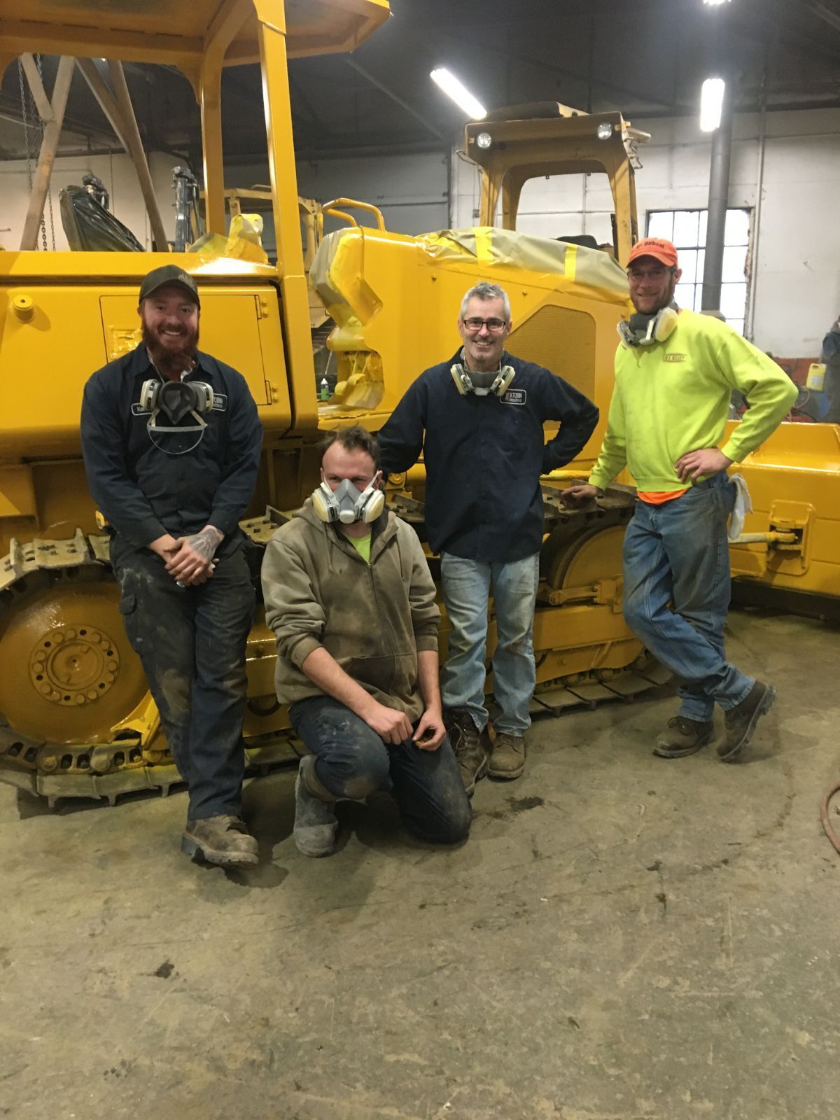 a group of men are posing for a picture in front of a yellow bulldozer .