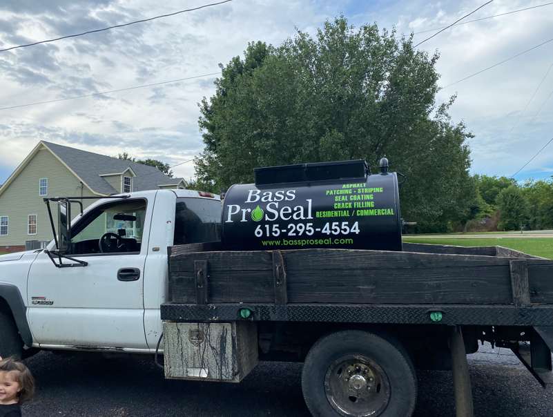 A white flatbed work truck with a black storage tank labeled 