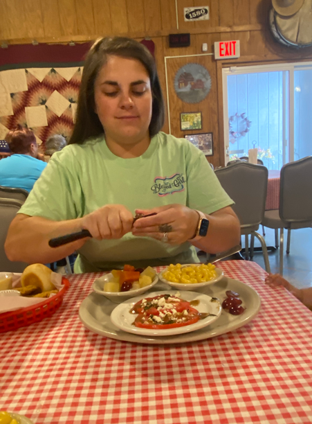 A person in a light green shirt cuts food at a table with a red-and-white checkered cloth in a restaurant setting.