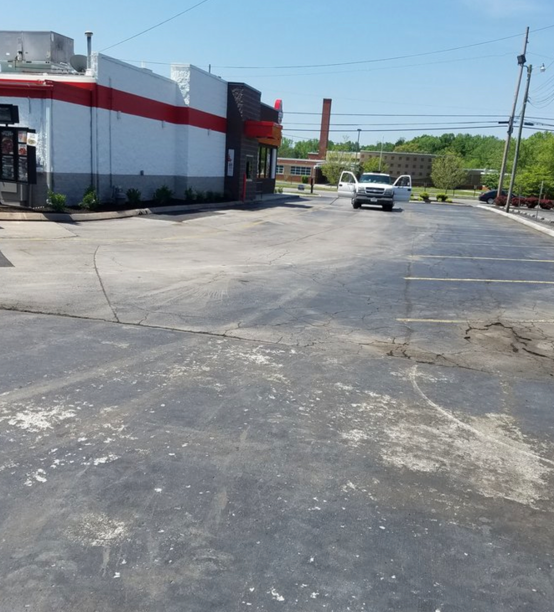 A white, red, and gray restaurant building sits next to an asphalt parking lot with a silver car parked in the distance.