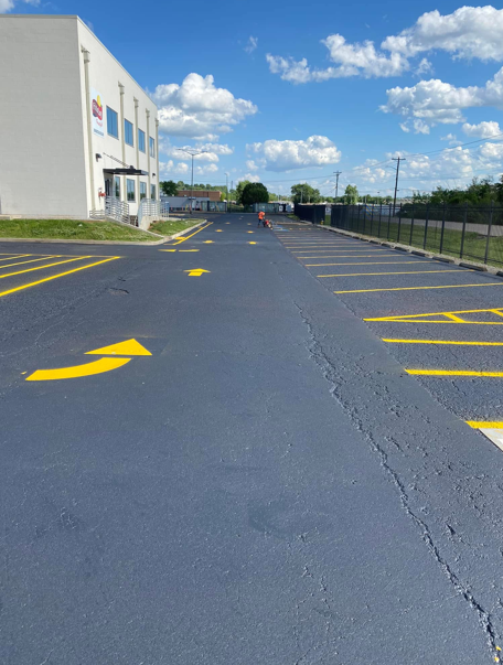 A parking lot with freshly painted yellow arrows and lines on the asphalt next to a white building under a blue sky.