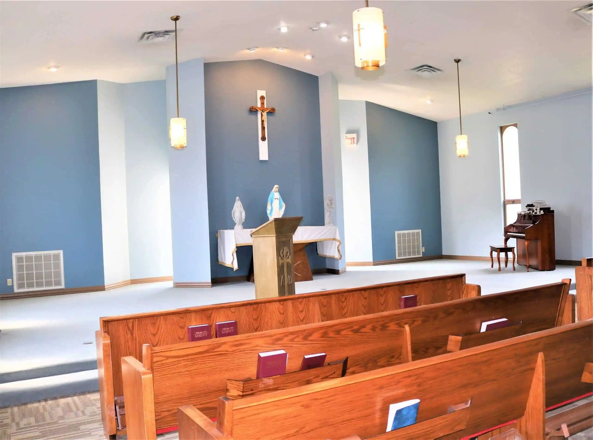 Interior of a chapel with light blue walls, wooden pews, a crucifix, and an organ.