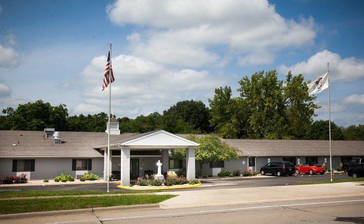 Long, one-story building with flags, cars, and trees on a sunny day.