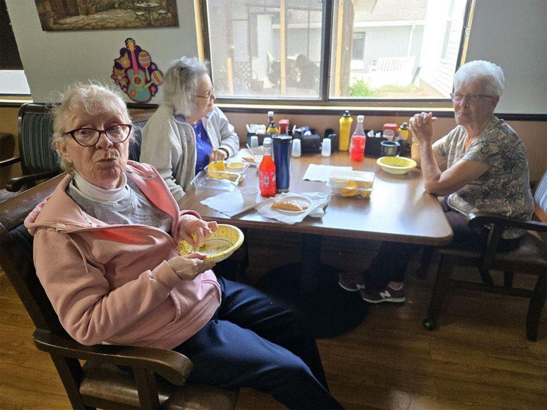 Three women seated at a table in a restaurant. One woman holds a plate, others look on.