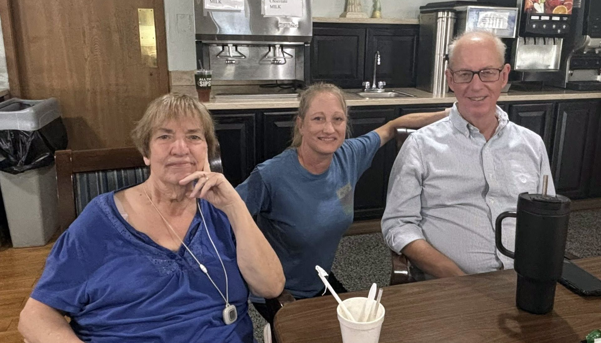 Three people seated at a table. Woman in blue top, another in a blue shirt leans in, man in button-down shirt smiles.